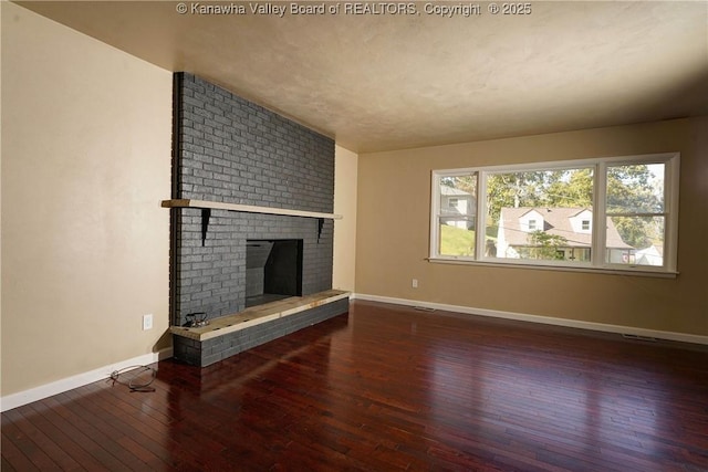 unfurnished living room featuring a brick fireplace and dark hardwood / wood-style floors