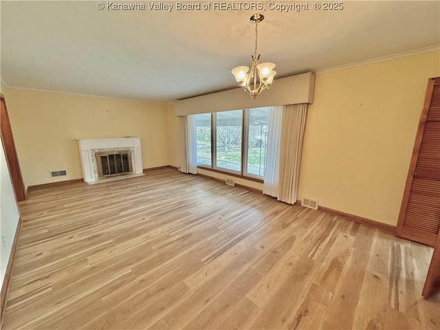 unfurnished living room with light wood-type flooring, a premium fireplace, a notable chandelier, and crown molding