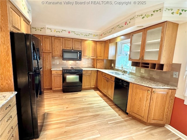 kitchen with light wood-type flooring, light stone countertops, black appliances, and tasteful backsplash