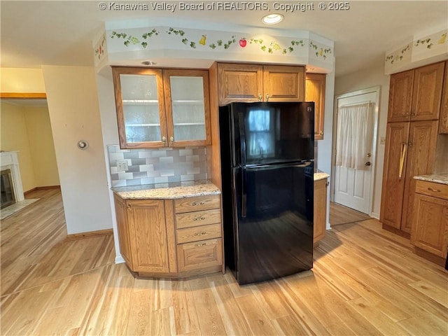 kitchen featuring tasteful backsplash, light stone countertops, light hardwood / wood-style floors, and black fridge