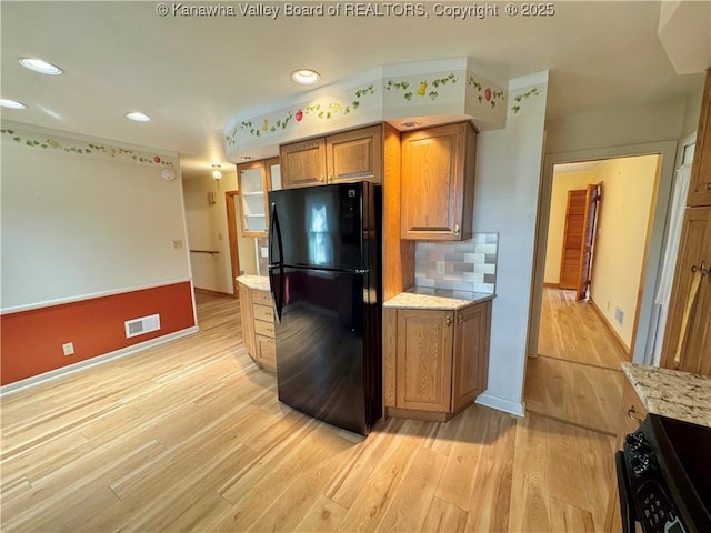 kitchen featuring light hardwood / wood-style floors, light stone countertops, black appliances, and decorative backsplash