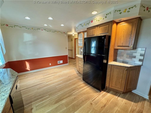 kitchen featuring decorative backsplash, light hardwood / wood-style floors, light stone counters, and black fridge