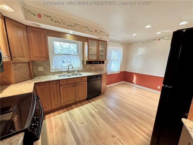 kitchen with light wood-type flooring, light stone counters, black appliances, decorative backsplash, and sink