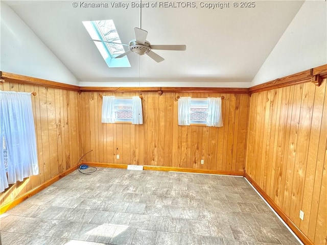 empty room with lofted ceiling, ceiling fan, wood walls, and a wealth of natural light