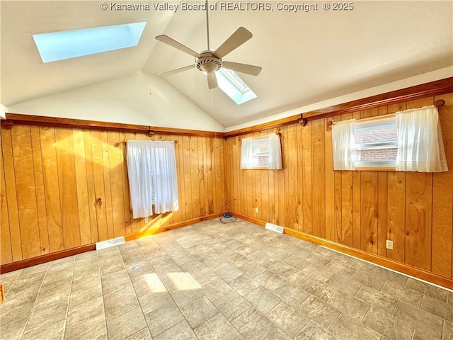 spare room with vaulted ceiling with skylight, ceiling fan, a healthy amount of sunlight, and wooden walls