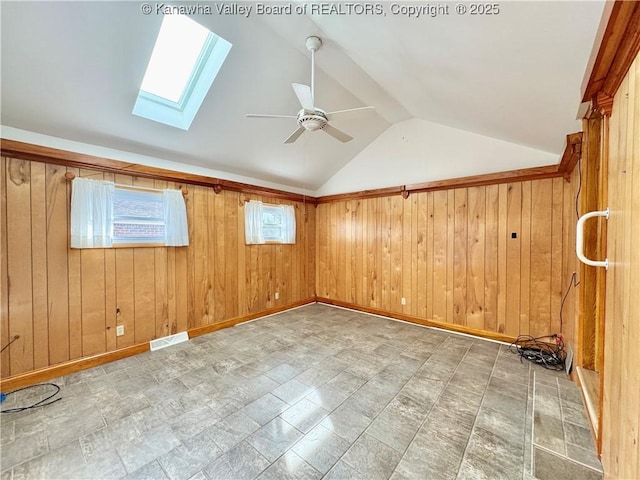 unfurnished room with ceiling fan, vaulted ceiling with skylight, and wooden walls