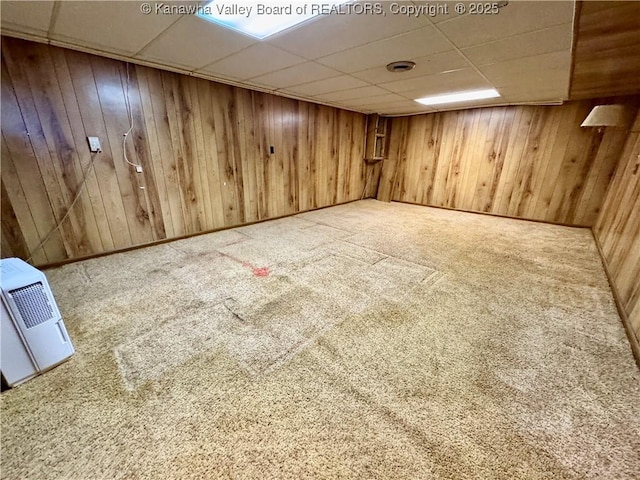 basement featuring wooden walls, a paneled ceiling, and carpet floors