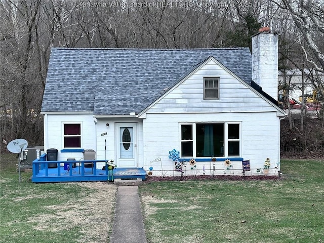 view of front facade with a shingled roof, a chimney, a wooden deck, and a front yard