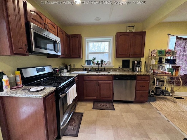 kitchen featuring appliances with stainless steel finishes, a sink, and light stone counters