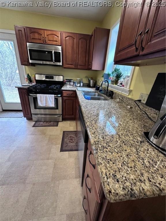 kitchen featuring stainless steel appliances, stone counters, and a sink