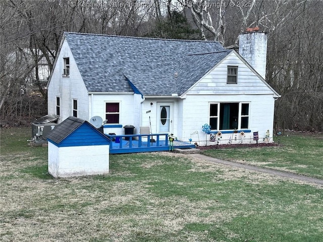 view of front facade featuring a shingled roof, a chimney, a deck, cooling unit, and a front yard