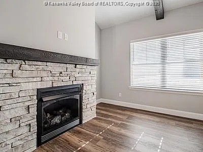 unfurnished living room with dark wood-type flooring, a fireplace, beam ceiling, and baseboards