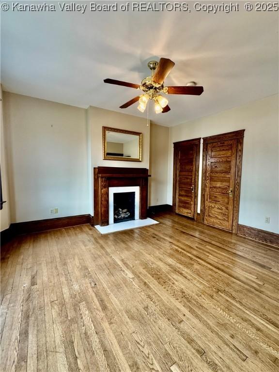 unfurnished living room with a fireplace with flush hearth, light wood-type flooring, ceiling fan, and baseboards