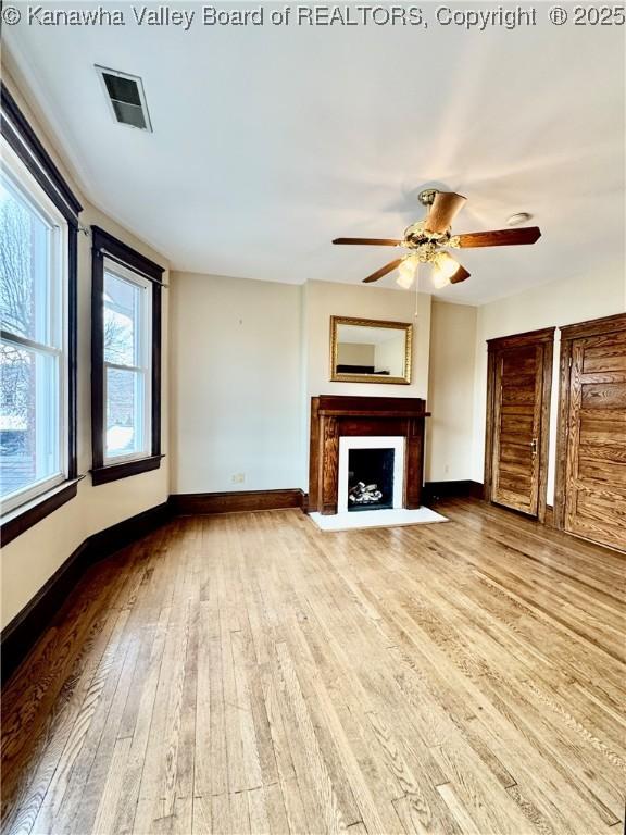 unfurnished living room featuring a fireplace with flush hearth, visible vents, baseboards, and wood finished floors