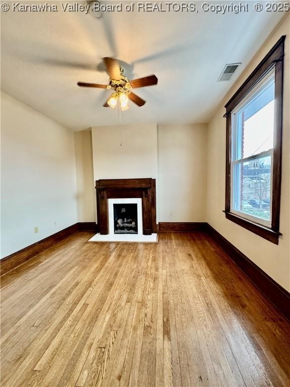 unfurnished living room featuring a fireplace with flush hearth, a ceiling fan, visible vents, baseboards, and light wood-type flooring