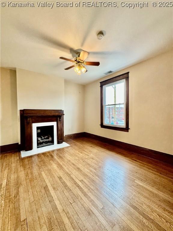 unfurnished living room featuring light wood-type flooring, a fireplace with flush hearth, and baseboards