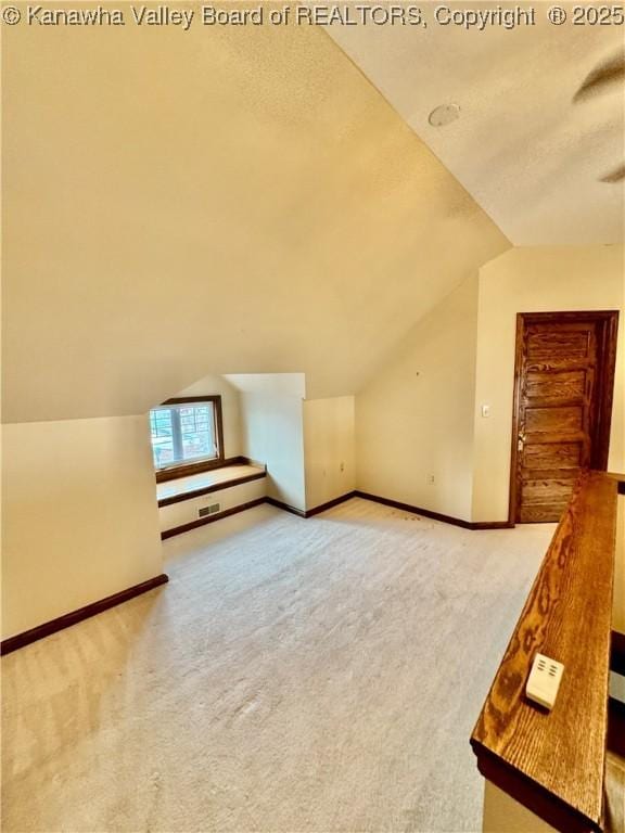 bonus room with light carpet, vaulted ceiling, a textured ceiling, and baseboards