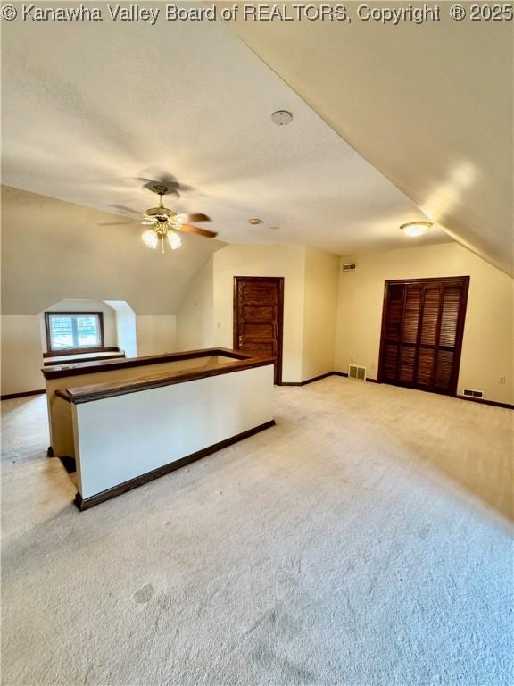 interior space featuring lofted ceiling, light colored carpet, visible vents, ceiling fan, and baseboards