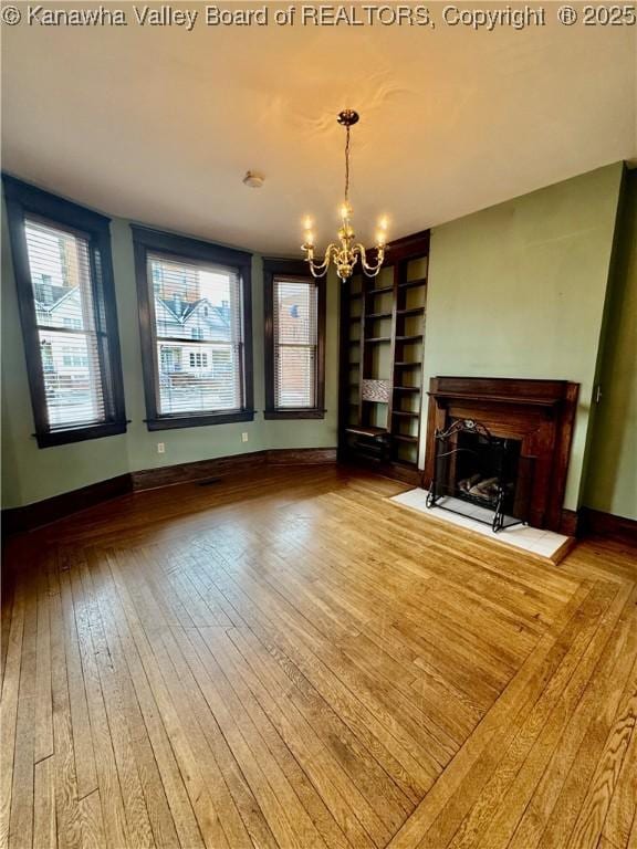 unfurnished living room featuring a fireplace with flush hearth, baseboards, light wood-style flooring, and a chandelier