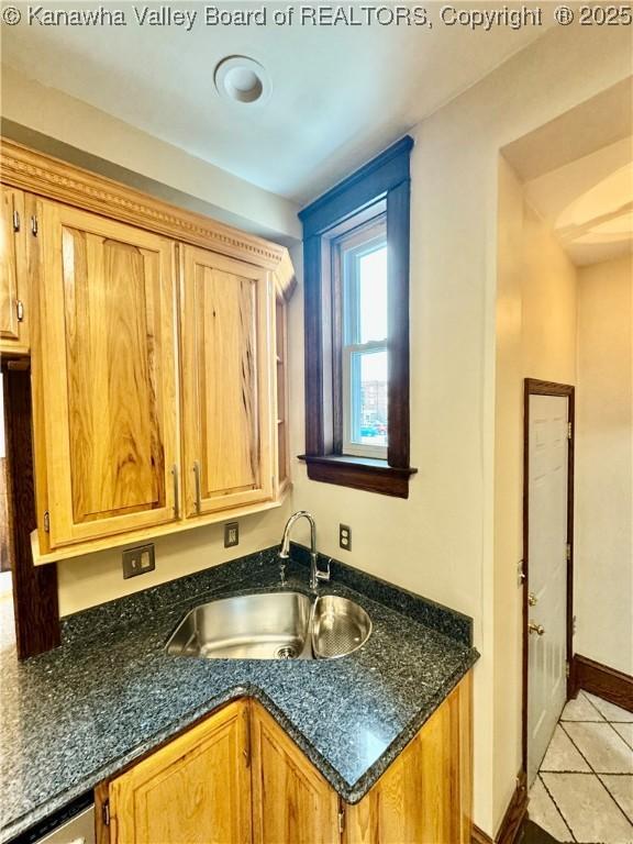 kitchen with brown cabinets, light tile patterned floors, stainless steel dishwasher, a sink, and dark stone countertops