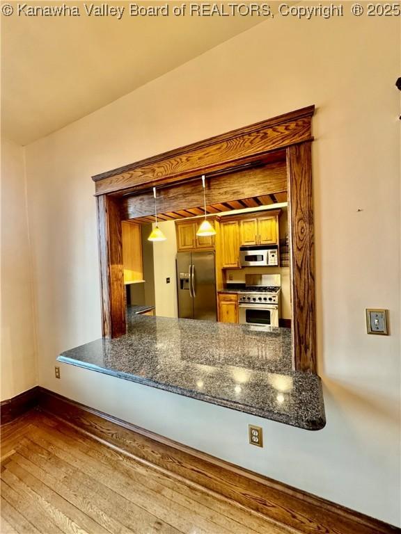 kitchen with brown cabinets, stainless steel appliances, hanging light fixtures, wood finished floors, and a peninsula