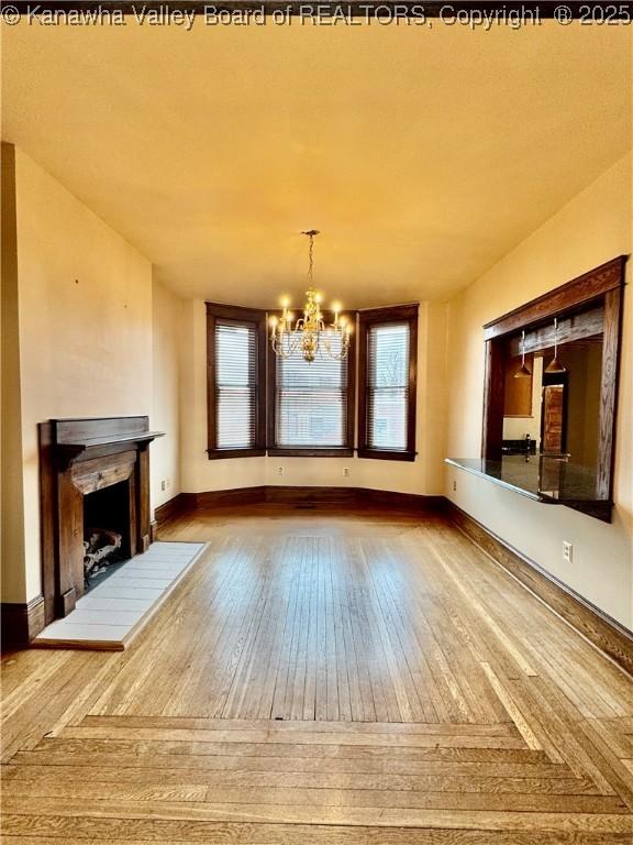 unfurnished living room featuring an inviting chandelier, a fireplace, baseboards, and wood finished floors