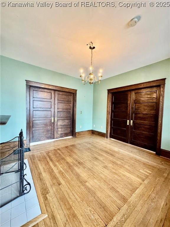 unfurnished bedroom with baseboards, light wood finished floors, and an inviting chandelier