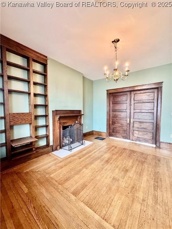 unfurnished living room with a fireplace with flush hearth, baseboards, an inviting chandelier, and wood finished floors