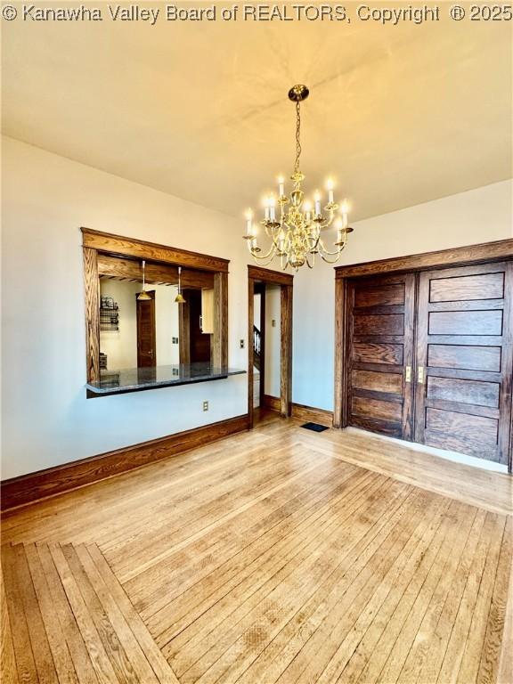 unfurnished dining area with light wood-style flooring, visible vents, baseboards, and a notable chandelier