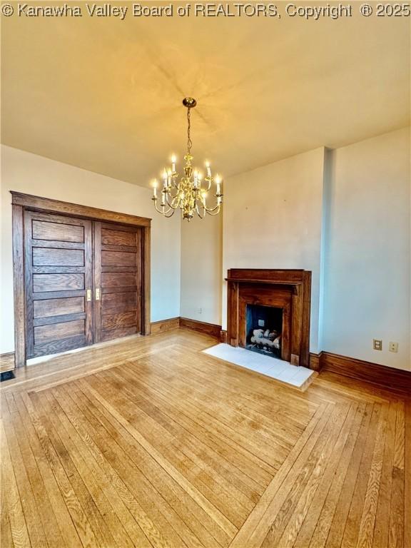 unfurnished living room with a chandelier, a fireplace, wood finished floors, and baseboards