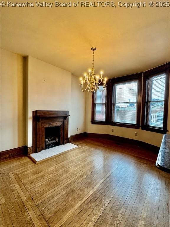 unfurnished living room with a fireplace with flush hearth, dark wood-style flooring, a chandelier, and baseboards