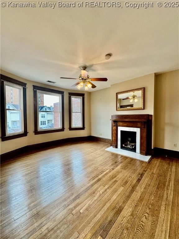 unfurnished living room featuring a ceiling fan, a fireplace with flush hearth, baseboards, and wood finished floors