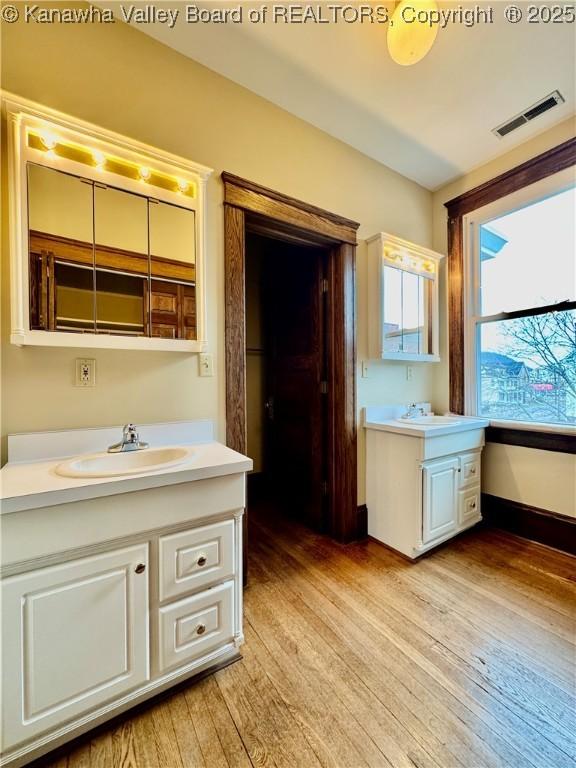 bathroom with wood finished floors, two vanities, a sink, and visible vents