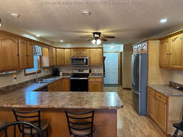 kitchen with a peninsula, a breakfast bar, a sink, appliances with stainless steel finishes, and dark countertops