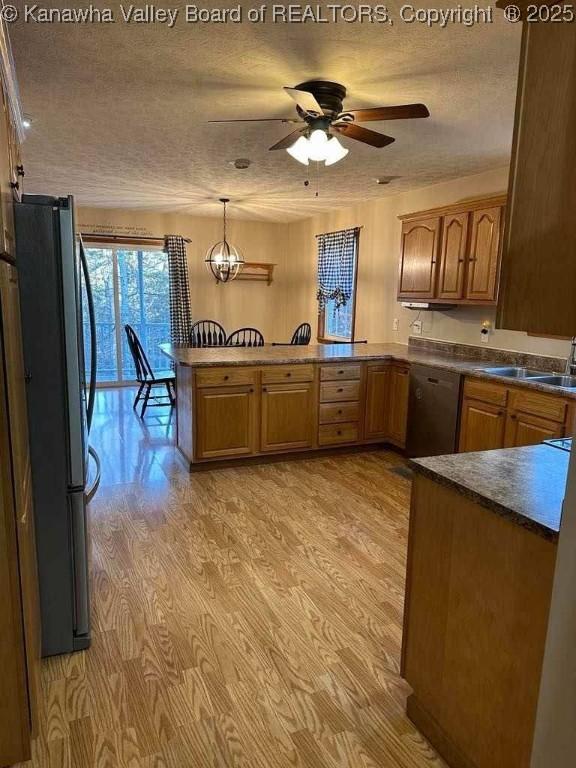 kitchen featuring a peninsula, light wood-style floors, appliances with stainless steel finishes, brown cabinets, and pendant lighting