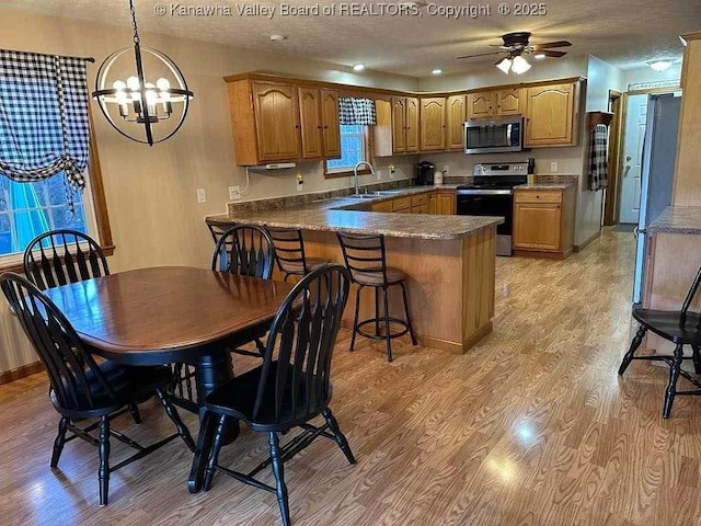 kitchen with light wood finished floors, dark countertops, appliances with stainless steel finishes, brown cabinetry, and a peninsula