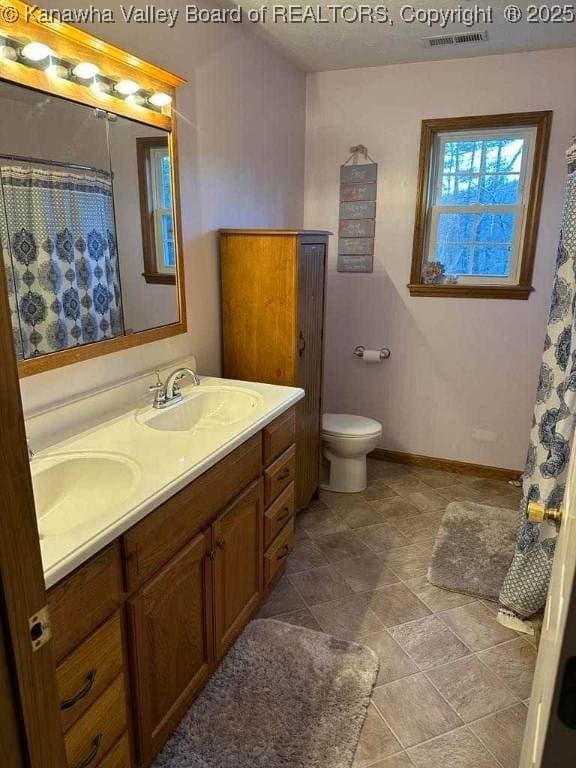 full bathroom with baseboards, a sink, toilet, and double vanity