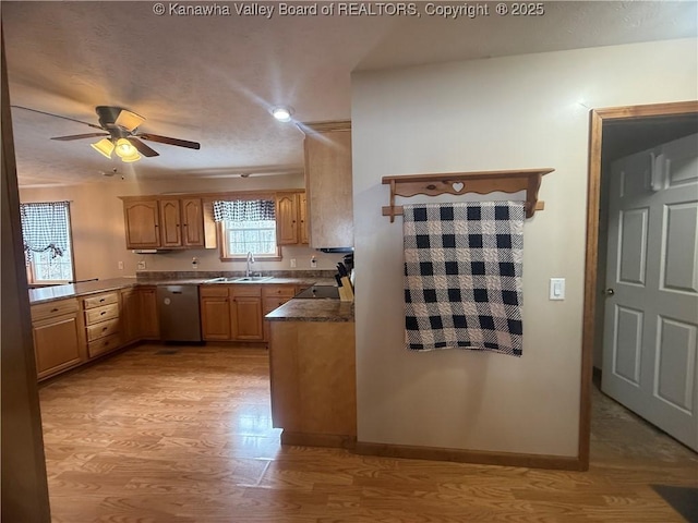 kitchen featuring dishwasher, dark countertops, a sink, and light wood-style floors