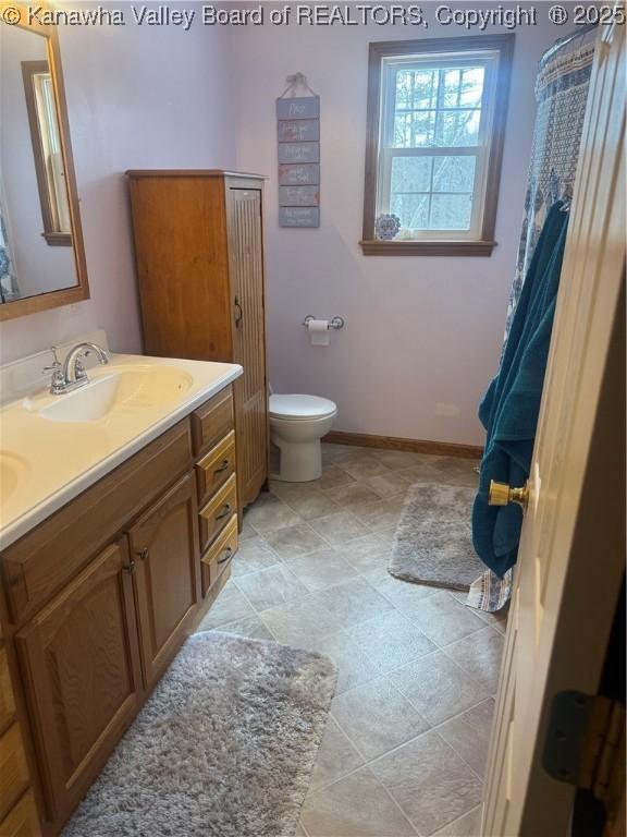 bathroom with toilet, double vanity, baseboards, and a sink