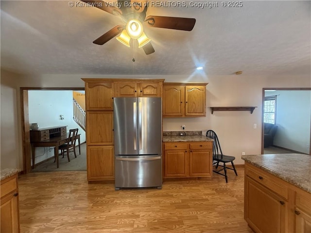 kitchen with a ceiling fan, brown cabinetry, freestanding refrigerator, and light wood-style floors