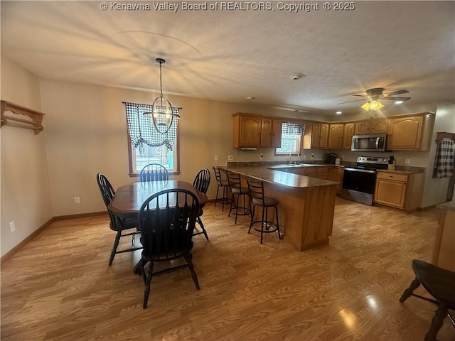 kitchen featuring pendant lighting, light wood finished floors, stainless steel appliances, dark countertops, and a sink