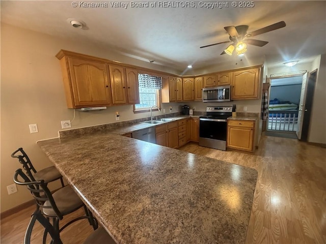 kitchen featuring a breakfast bar area, dark countertops, appliances with stainless steel finishes, a sink, and a peninsula