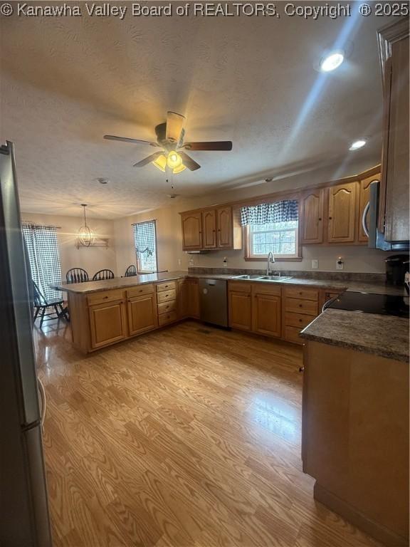 kitchen with a peninsula, hanging light fixtures, brown cabinetry, and stainless steel appliances