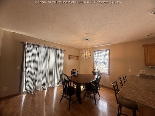 dining area with a notable chandelier, a textured ceiling, baseboards, and wood finished floors