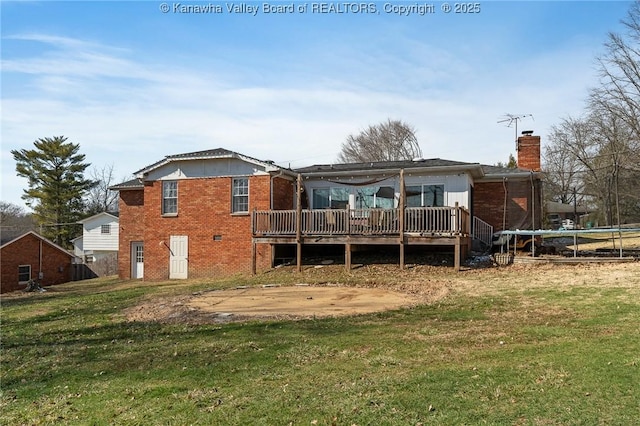 rear view of property featuring a lawn, a chimney, a trampoline, a wooden deck, and brick siding