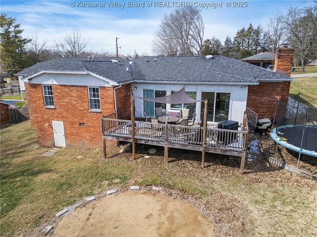 rear view of house featuring a deck, brick siding, a trampoline, and a lawn