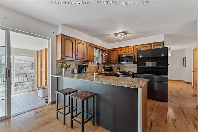 kitchen featuring light wood-style flooring, stainless steel appliances, a peninsula, brown cabinets, and tasteful backsplash