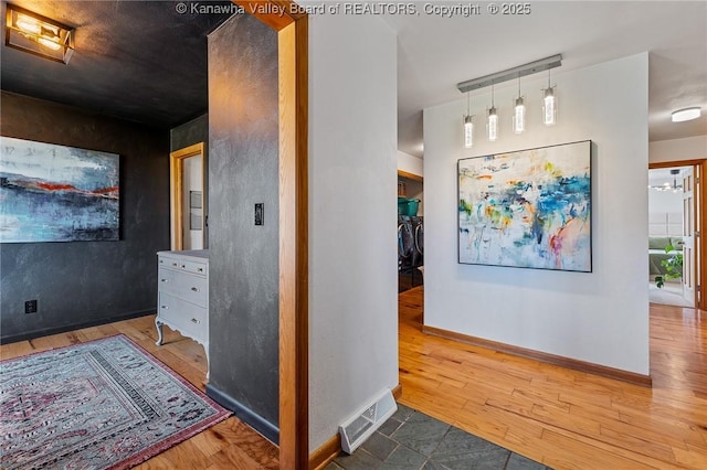 corridor with baseboards, visible vents, and wood finished floors