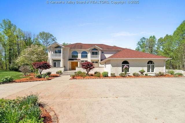 mediterranean / spanish home featuring driveway, brick siding, and a balcony