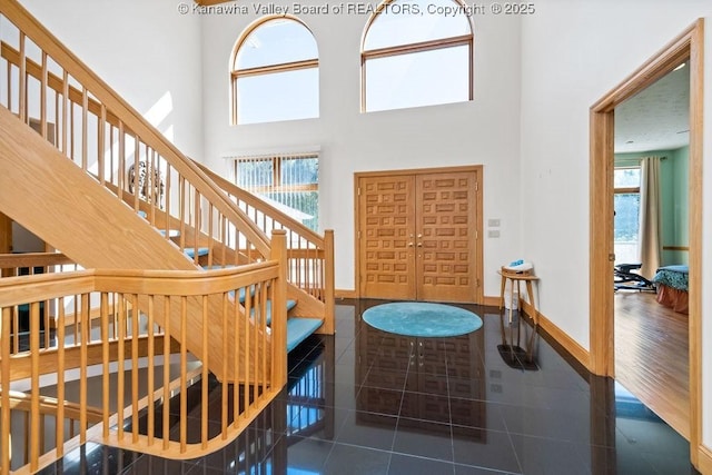 foyer entrance featuring stairway, dark tile patterned flooring, a towering ceiling, and baseboards